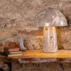 Decorative table lamp with a stone-like finish on a wooden table against a stone wall.