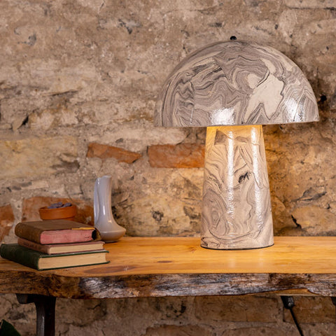 Decorative table lamp with a stone-like finish on a wooden table against a stone wall.